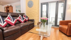 A living room with a brown leather sofa, a glass coffee table, and a vase with flowers.