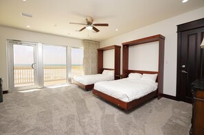 Quarto com duas camas, ventilador de teto e vista para a praia através de grandes portas de correr.