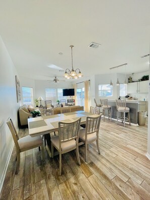 A spacious living area with a dining table, chairs, a sofa, and a kitchen area with bar stools.