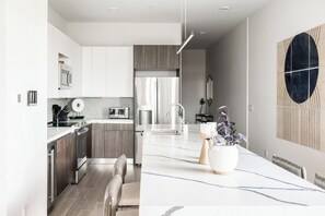 A modern kitchen with a central island, stainless steel appliances, and a dining area with a large table. - Denver Skyline Views | Walk to Empower Field (Denver)