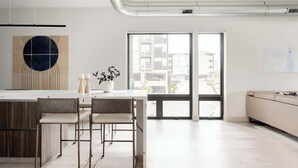A modern kitchen with a central island, a dining area with chairs, and a large window with a city view. - Denver Skyline Views | Walk to Empower Field (Denver)
