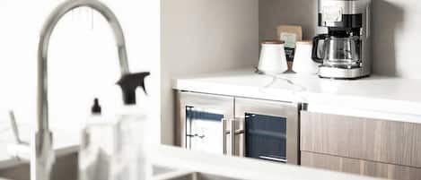 A modern kitchen with a stainless steel sink, a coffee maker, and a cabinet.