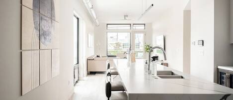 A modern kitchen with a marble countertop, a built-in oven, and a large window providing natural light.