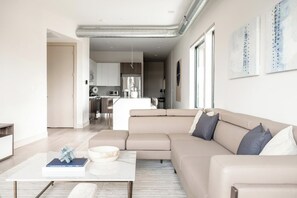 A modern living room with a beige sectional sofa, a coffee table, and a kitchen in the background. - Denver Skyline Views | Walk to Empower Field (Denver)