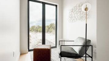 A modern room with a large window, a floor lamp, a grey chair, and a textured ottoman.