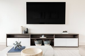 A modern living room with a flat-screen TV mounted on the wall, a wooden coffee table, and a minimalist console table with decorative items. - Denver Skyline Views | Walk to Empower Field (Denver)