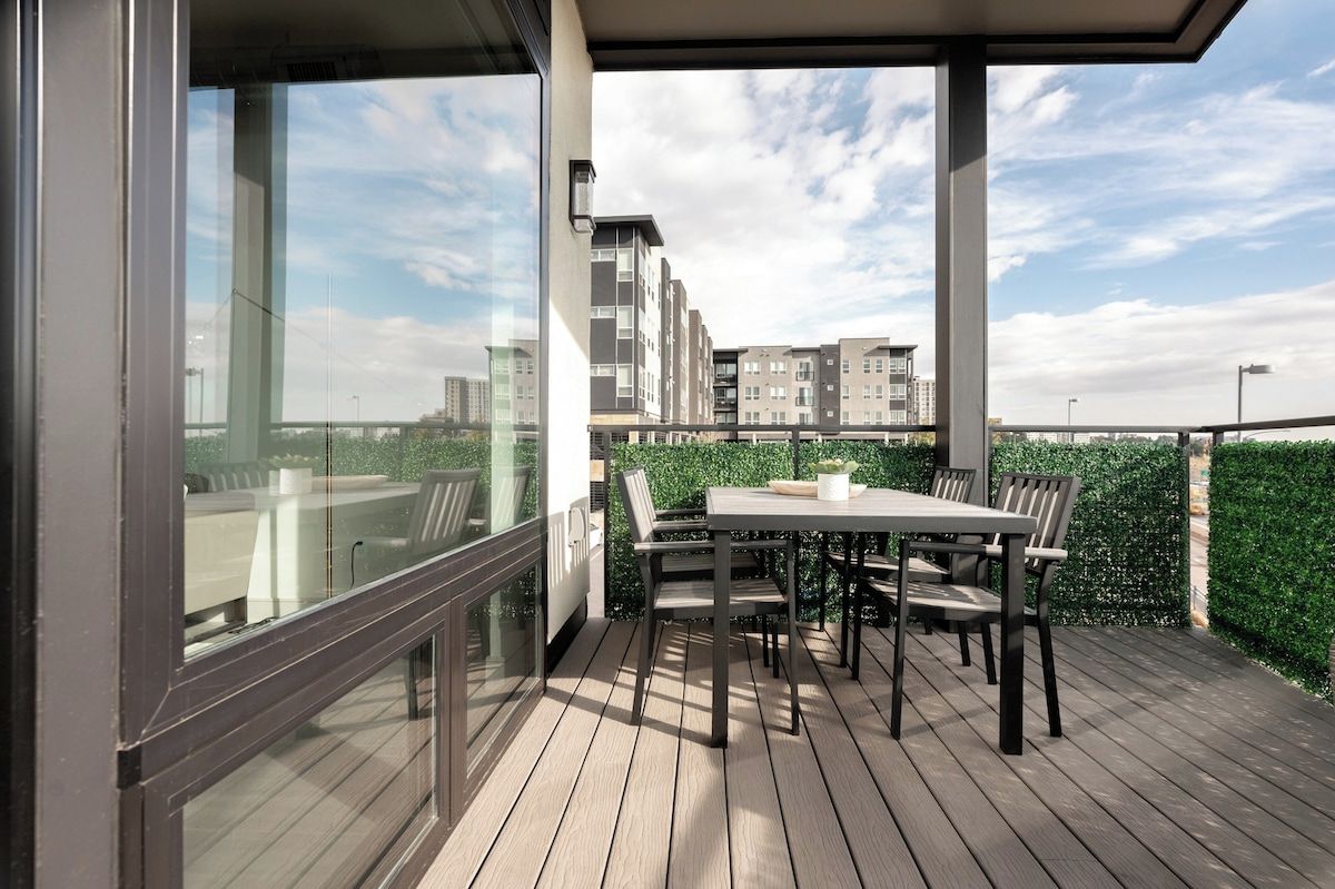 A balcony with a table and chairs, overlooking a cityscape with buildings and a bridge.