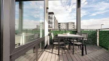 A balcony with a table and chairs, overlooking a cityscape with buildings and a bridge.