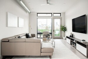 A modern living room with a sectional sofa, a flat-screen TV, and a balcony with a city view. - Denver Skyline Views | Walk to Empower Field (Denver)