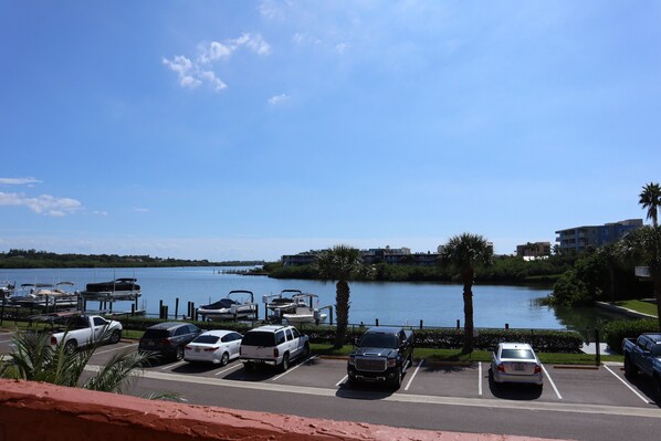 Un estacionamiento con varios coches y barcos junto a un lago, rodeado de vegetación y edificios.