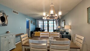 A dining area with a wooden table and chairs, a chandelier, and a view through large windows. - 4 Minute Walk to Beach! Waterfront and Pool View-Indian Shores Beach! (Indian Shores)