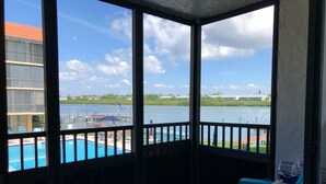 A balcony with a view of a swimming pool and a dock extending into a body of water. - 4 Minute Walk to Beach! Waterfront and Pool View-Indian Shores Beach! (Indian Shores)