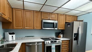A modern kitchen with wooden cabinets, stainless steel appliances, a microwave, a refrigerator, and a dishwasher. - 4 Minute Walk to Beach! Waterfront and Pool View-Indian Shores Beach! (Indian Shores)