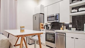 Una cocina compacta con muebles blancos, un refrigerador de acero inoxidable, un microondas, un horno y un lavavajillas.