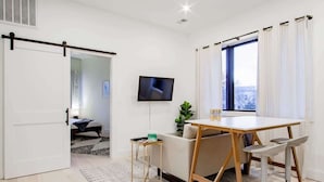 Una sala de estar moderna con un sofá, una mesa de centro, un televisor y una puerta corredera que da a otra habitación.