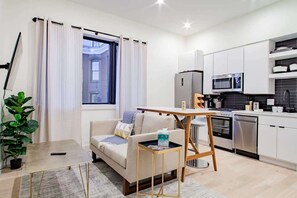 A modern apartment with a kitchenette, a sofa, a small table, and a potted plant. - Eastern Market & METRO Accessible, Modern Charm, Walk Everywhere! (Washington)