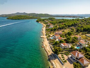 An aerial view of a coastal residential area with houses, a beach, and clear blue waters.