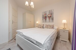 A bedroom with a bed, nightstands, a chandelier, a door, and a painting on the wall.
