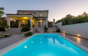 A modern house with a swimming pool, outdoor seating, and a covered patio.