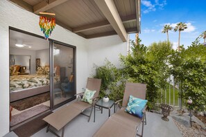 A bedroom with a bed, a window, and a balcony with seating and plants.
