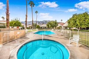 A swimming pool with a diving board, surrounded by palm trees and a mountainous backdrop.