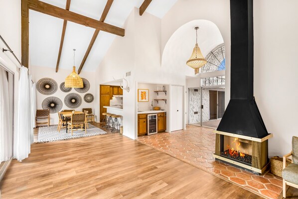 A spacious living area with a large fireplace, wooden flooring, and a high ceiling with exposed beams.