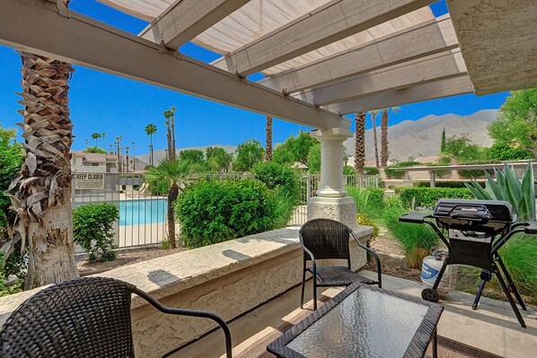 An outdoor patio area with a pool in the background, a grill, and a view of the mountains.