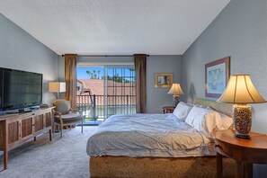 Habitación de hotel con una cama grande, televisión, escritorio con lámpara y vistas al balcón exterior.