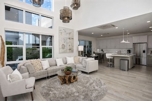 A modern interior with a sectional sofa, a glass coffee table, and a kitchen area with stainless steel appliances.