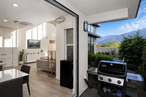Et moderne køkken med indbygget grill, et spiseområde med bord og stole, samt udsigt til bjerge gennem skydedøren.
