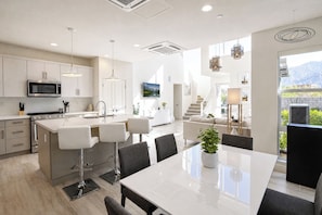 A modern kitchen with a central island, a dining area with a large table, and a staircase leading to an upper level.