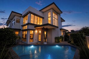 Et moderne hus med to etager, en swimmingpool, store vinduer og et godt oplyst ydre.