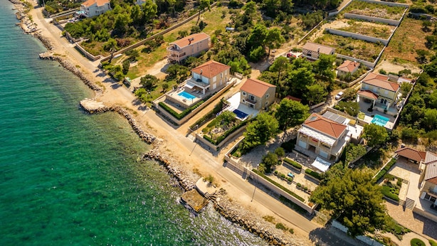 An aerial view of a coastal residential area with houses, a beach, and a bridge in the background.