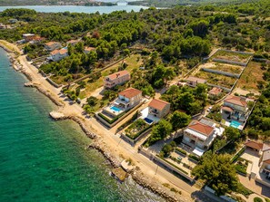 Vista aérea de una zona residencial costera con casas, una playa y un puente al fondo.