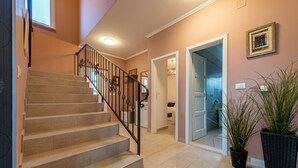 A staircase with beige steps and black railings leading to an upper floor. There are potted plants on the landing and a framed picture on the wall.
