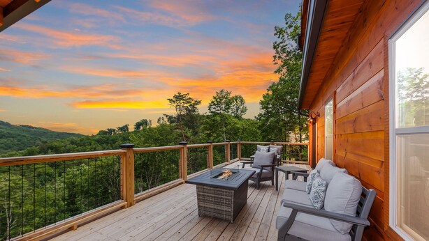 Une terrasse en bois, dotée de mobilier d’extérieur, d’un foyer et offrant une vue sur un paysage boisé.
