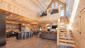 Une cabine spacieuse avec un intérieur en bois, un espace cuisine central, un coin repas et un escalier menant à un niveau supérieur.