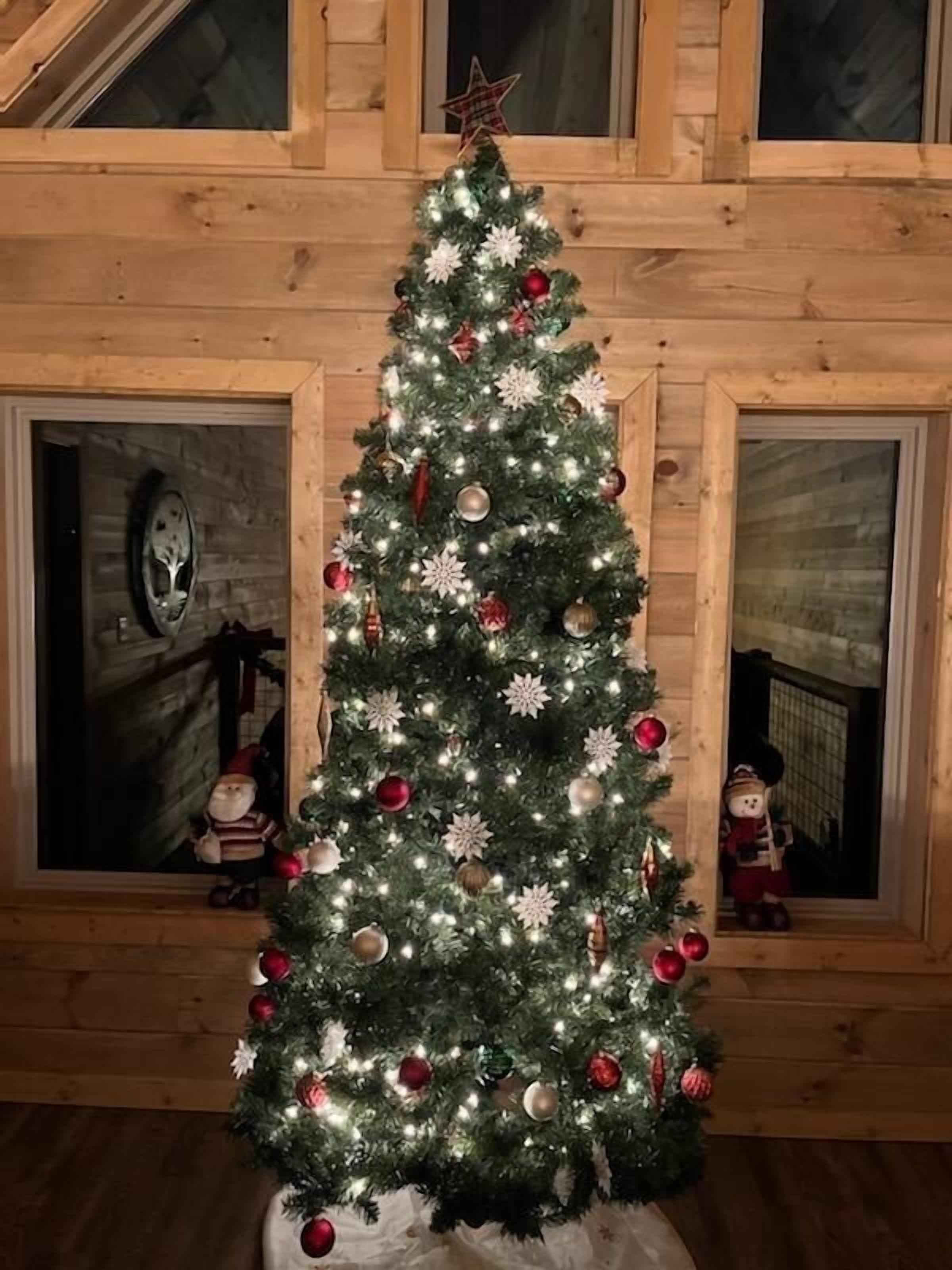 Un albero di Natale decorato con ornamenti e luci in una stanza in legno con finestre.