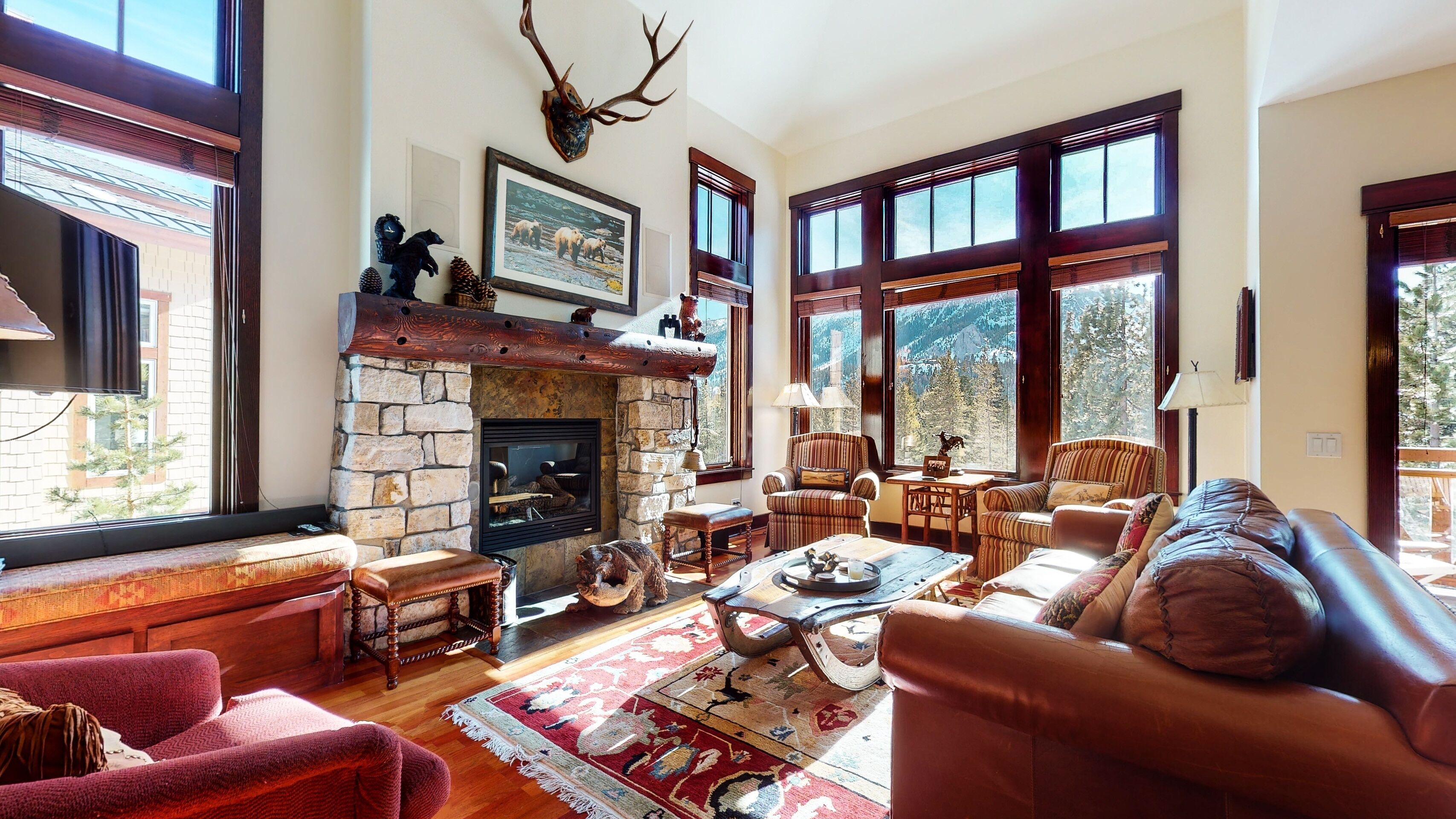 A cozy living room with a stone fireplace, large windows, and comfortable seating.