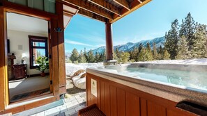 A wooden deck with a hot tub overlooking a snowy mountain landscape.