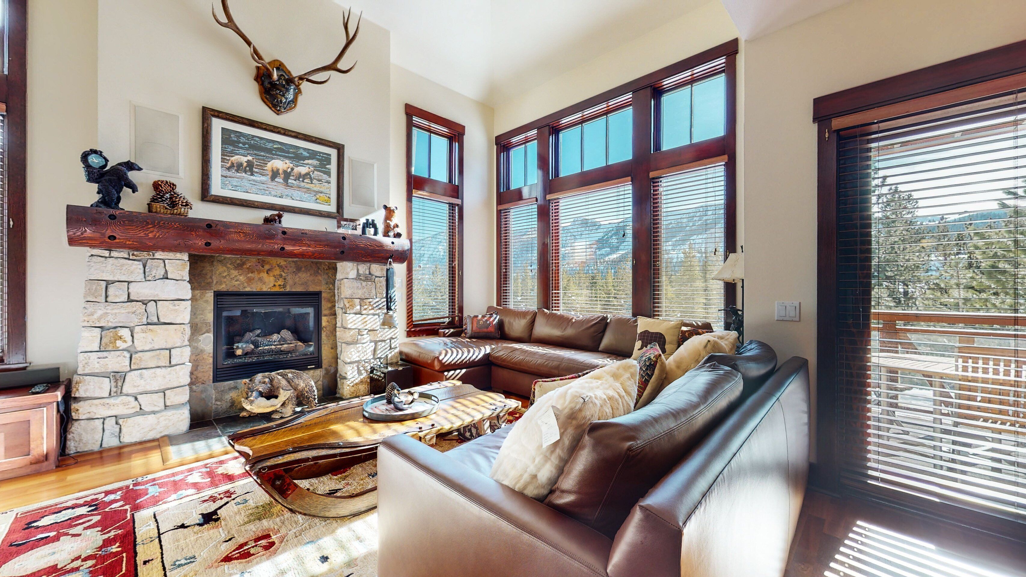 A cozy living room with a stone fireplace, leather sofa, and large windows.