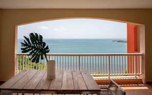 Enjoy ocean views from this balcony with a table, green plant, and vase.