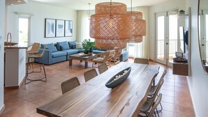 A spacious living area with a long wooden dining table, wicker chairs, a blue sofa, and a large woven pendant light.