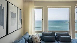 A room with a sofa, pillows, and large windows offering a view of the sea.