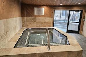 A hot tub with a metal grid floor, surrounded by beige tiles and wooden walls.