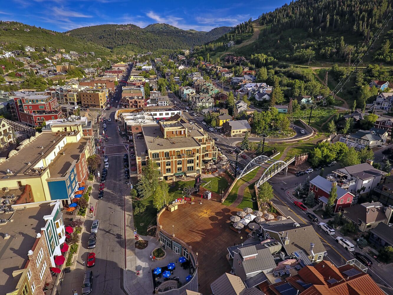 Aerial view of a charming mountain town nestled in a scenic valley, surrounded by forested peaks and natural landscape. The property is located in this vibrant neighborhood with local shops and dining nearby.