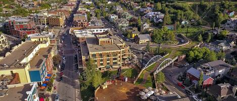 Aerial view of a charming mountain town nestled in a scenic valley, surrounded by forested peaks and natural landscape. The property is located in this vibrant neighborhood with local shops and dining nearby.