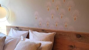 Una cama bien hecha con sábanas blancas y varios almohadones, cabecera de madera y pared con un diseño decorativo de abanicos.