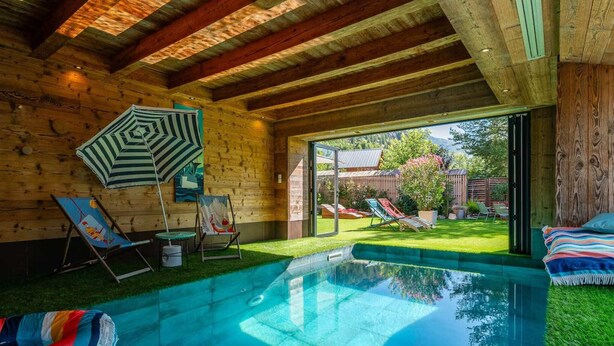 Una cabaña de madera con piscina, sillones de descanso y vista al jardín.