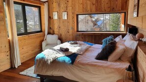Un dormitorio acogedor de cabaña de madera, con una cama, una silla, una ventana y vistas al exterior.